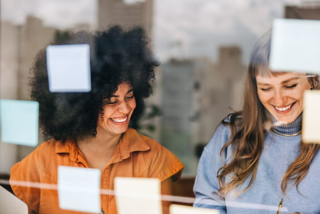 Cheerful young businesswomen brainstorming using sticky notes.