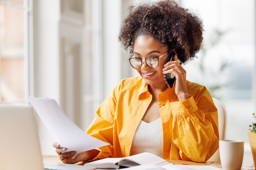 Black woman using cell phone and looking at paper