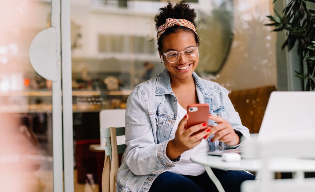 Black woman looking at phone with laptop on table